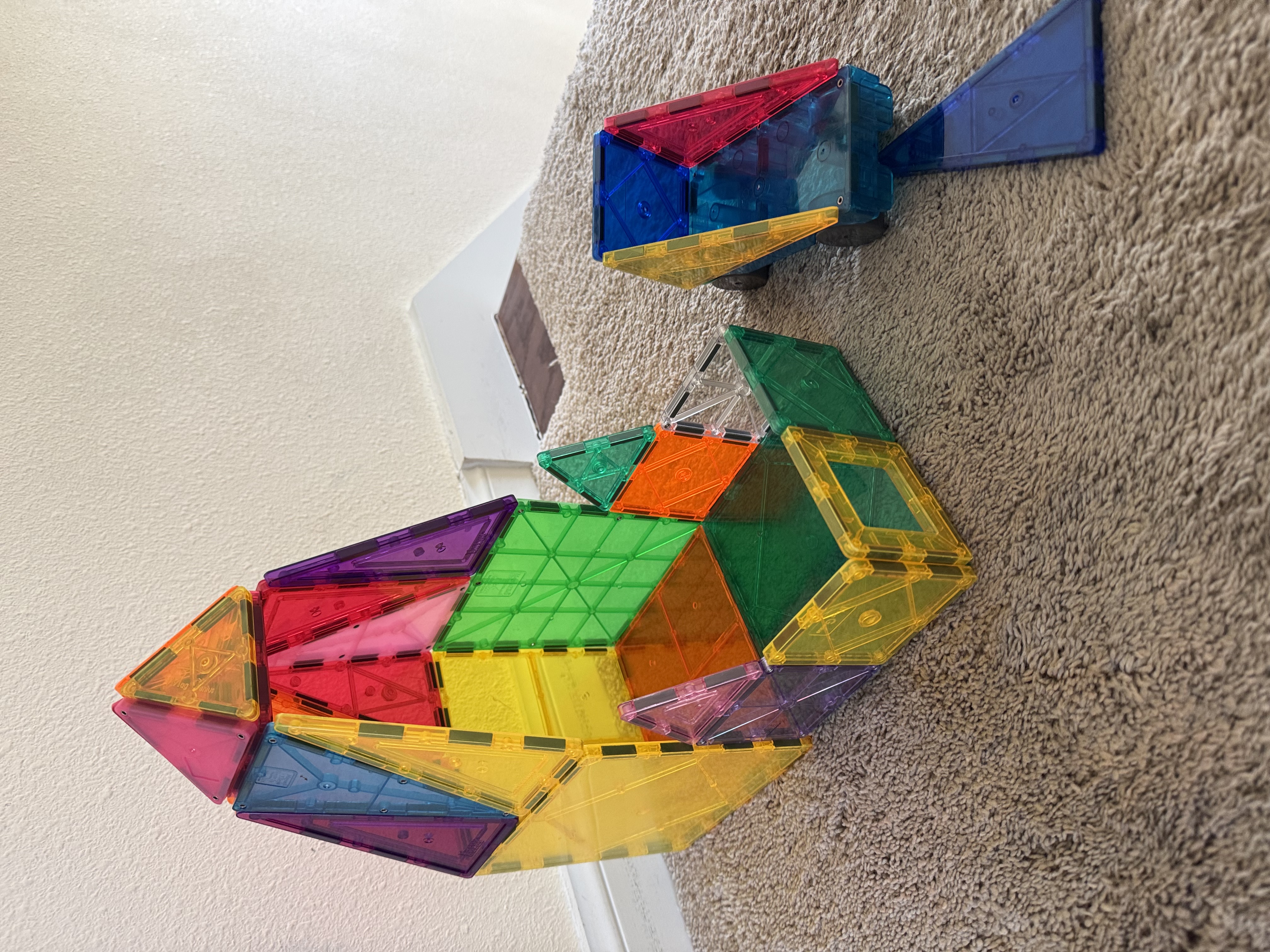 A colorful MagnaTiles construction on the floor — geometric shapes snapped together into a complete form